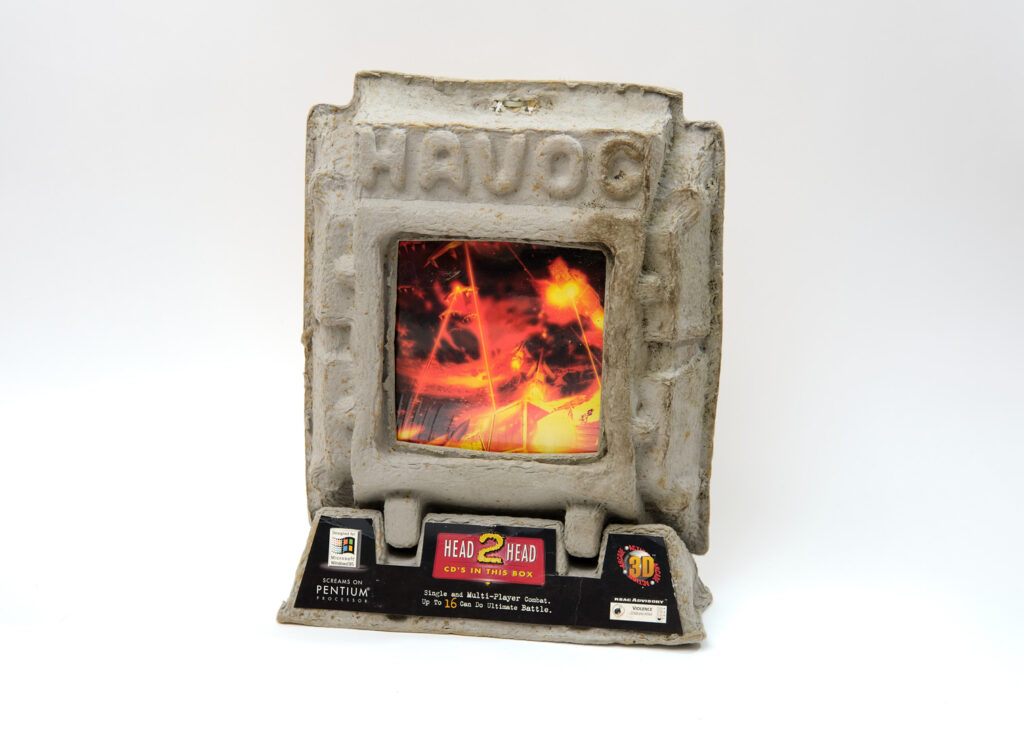 The box for Havoc. It is a large, distended, pulpy object shaped vaguely like a computer monitor. The box has clearly seen a great deal of wear and discoloration, although it's unclear how much of that was an intentional part of the design. On the monitor screen, there is a scene of fire and chaos. The bottom of the box includes a small advertisement for the game's features.