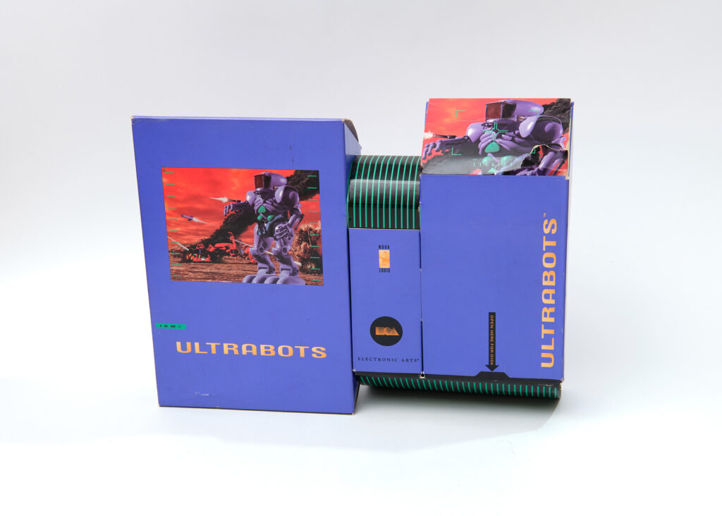 The box for Ultrabots. It consists of three differently-sized rectangular purple boxes stacked next to each other. The boxes are decorated with a combination of game art, featuring a large purple robot, and black-and-green cybernetic stripe patterns.